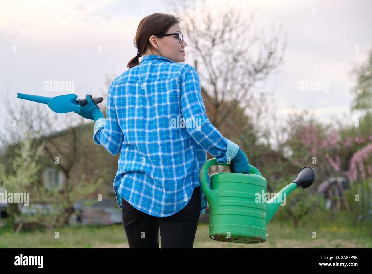 Female gardener holding watering can and garden tools Stock Photo - Alamy