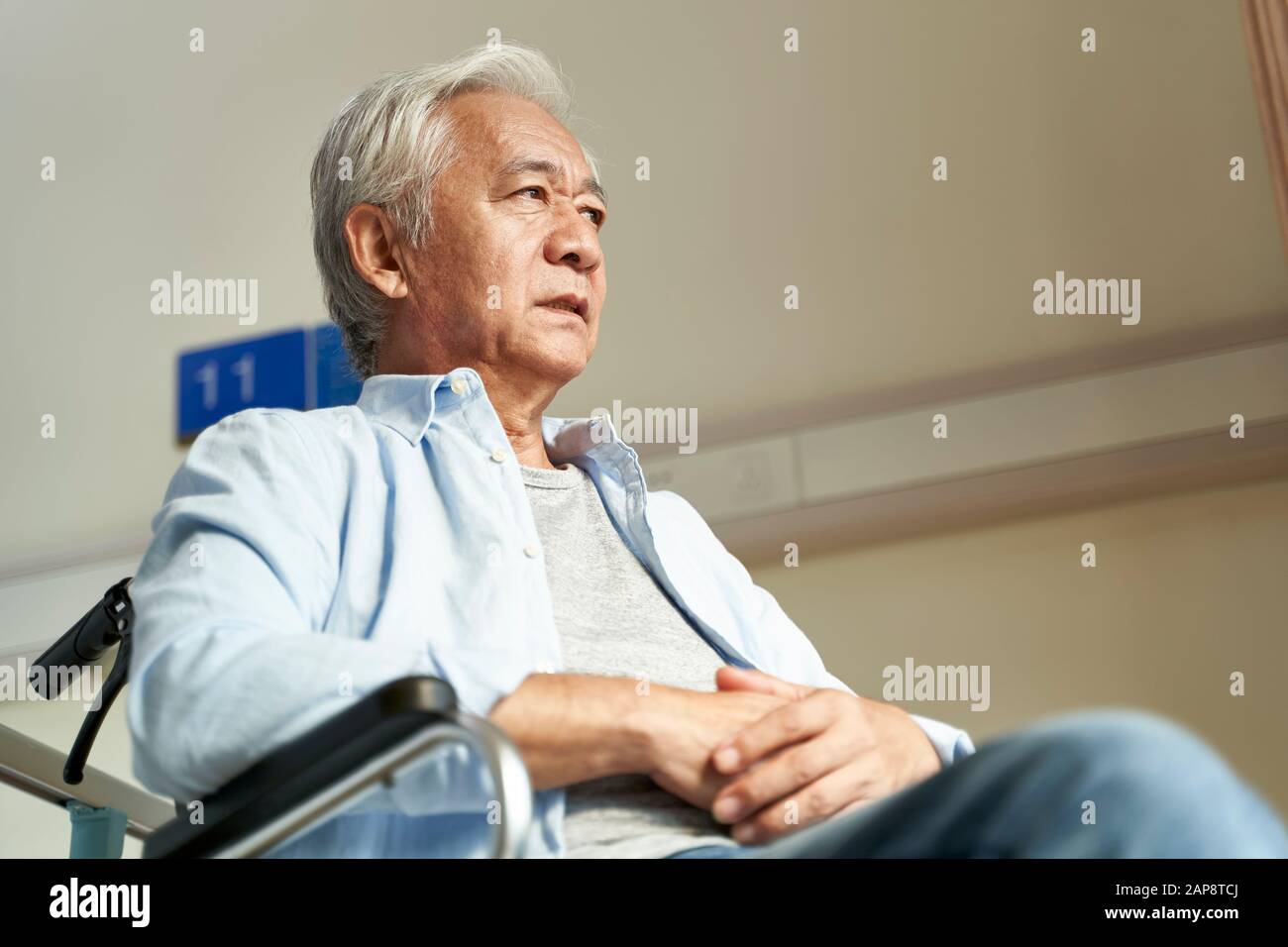 elderly asian man sitting in wheelchair in nursing home with serious facial expression Stock Photo