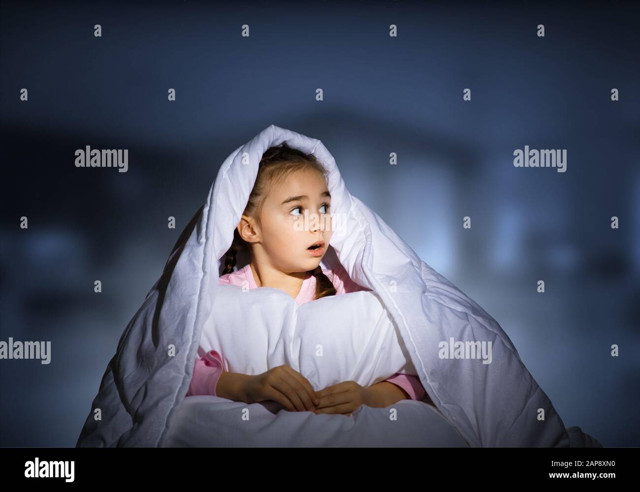 Scared girl with pillow hiding under blanket Stock Photo