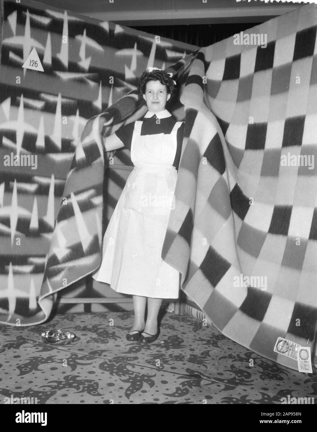 Dekenshow. Fa. van Wijk en Co NV Annotation: A young woman in nurse unifrom between blankets Date: 20 March 1957 Keywords: textile, textile industry Stock Photo