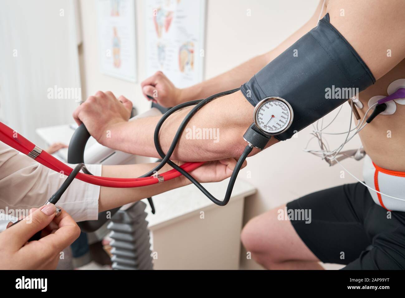 The nurse measures arterial tension. Man patient, pedaling on a bicycle ergometer stress test system for the function of heart checked. Athlete does a Stock Photo