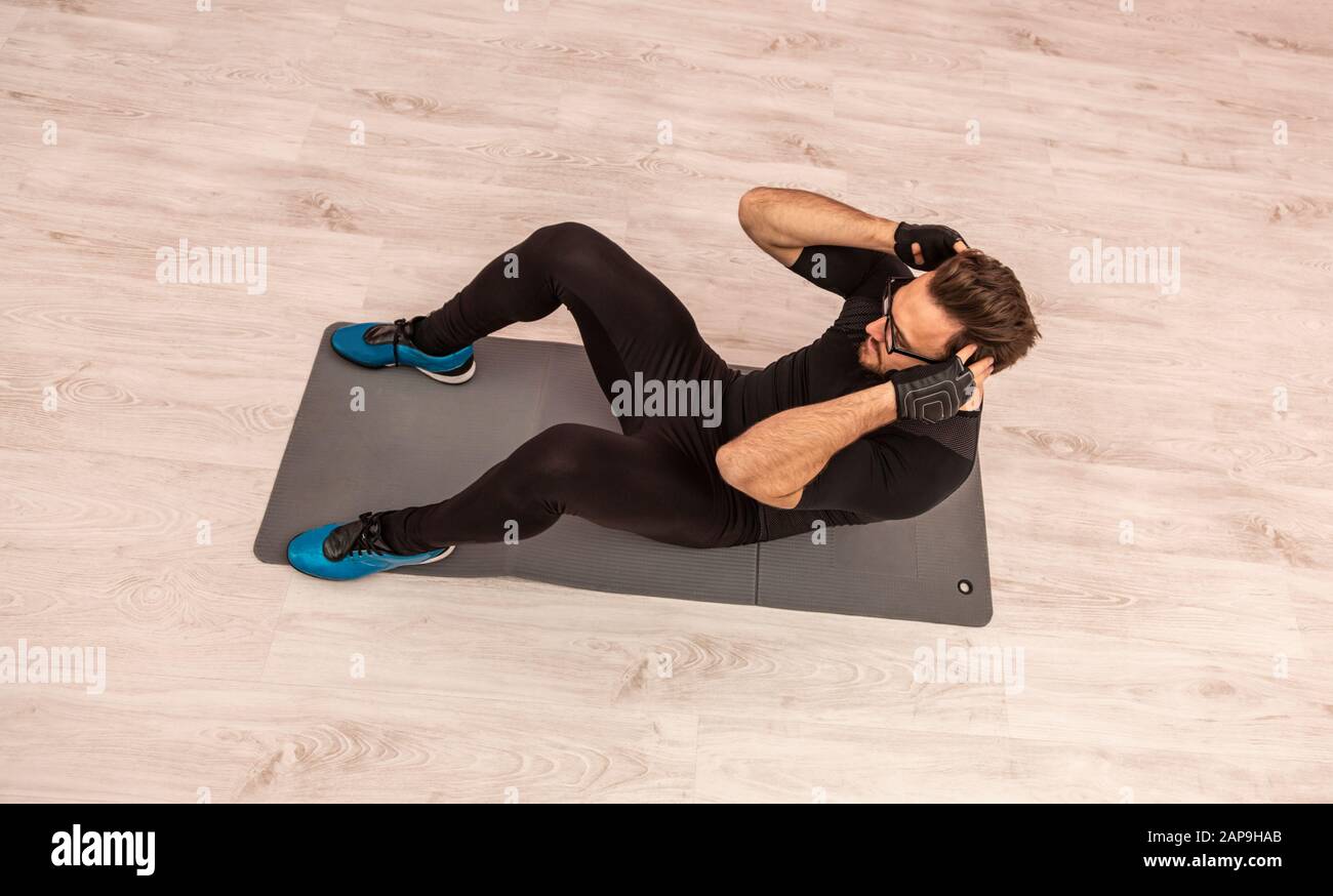 Bird eye view of a young man with spectacles doing situps on the floor