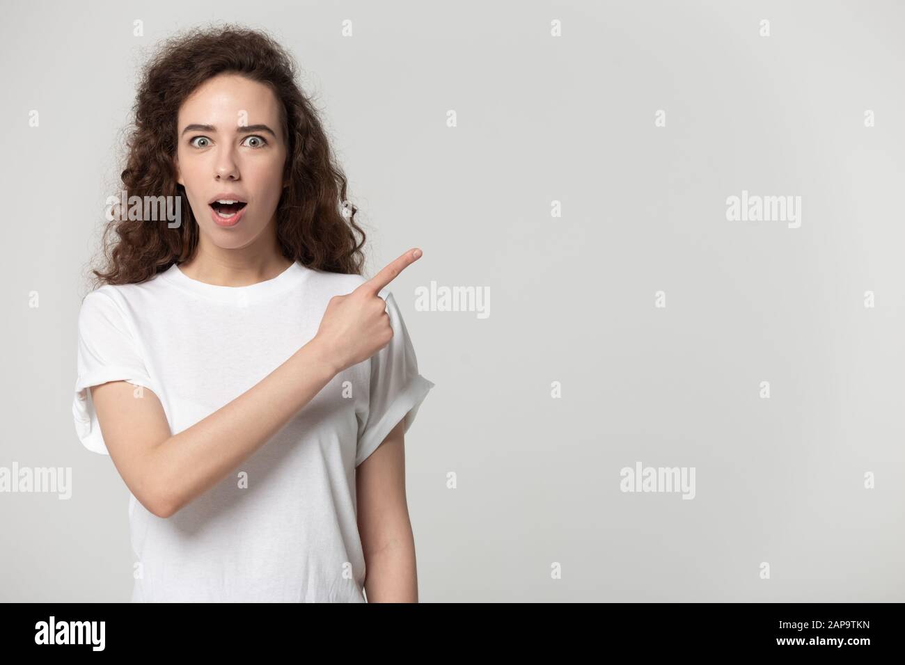 Surprised young girl standing aside, pointing finger to free space