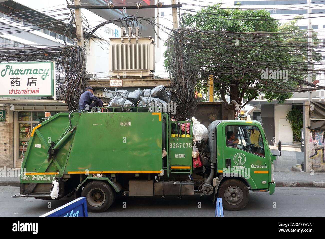Bangkok, Thailand - December 26, 2019: Green garbage truck. One worker sitting on the roof with many black plastic bags. Stock Photo