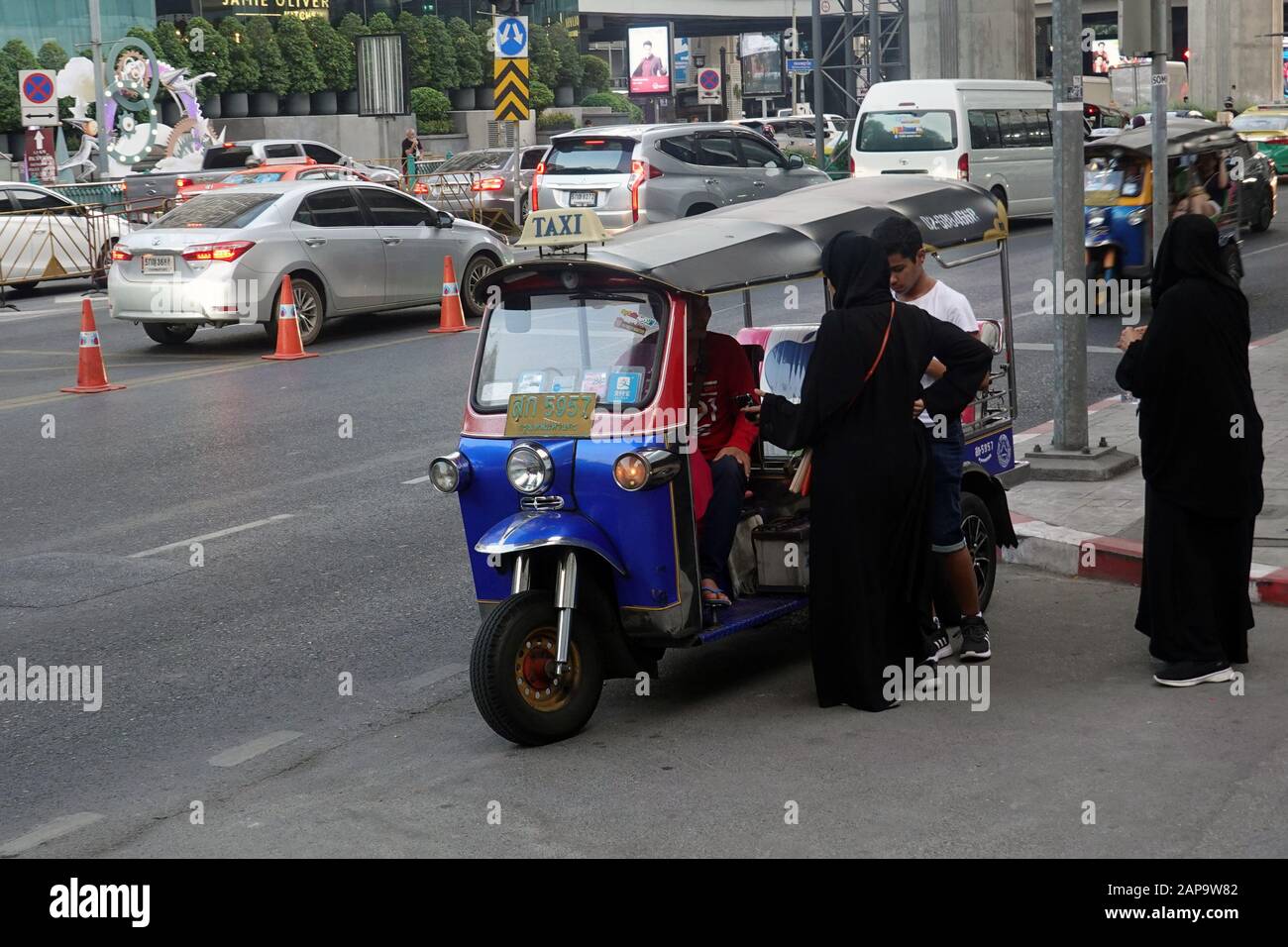 Bangkok, Thailand - December 21, 2019: Muslim women and boy negotiate with tuk tuk driver for transportation. Stock Photo