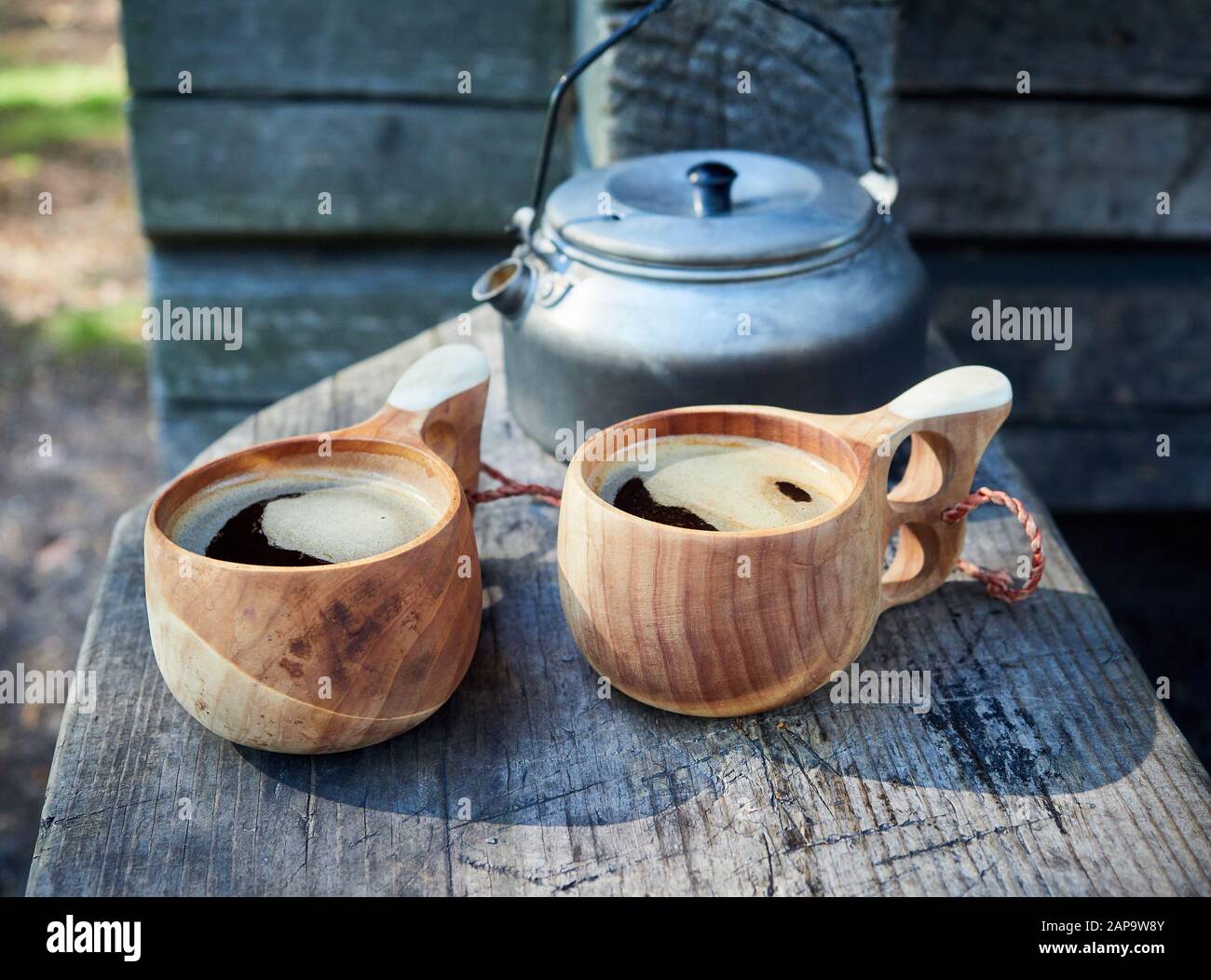 Two wooden mugs filled with hot fresh coffee on the campsite while trekking. Stock Photo