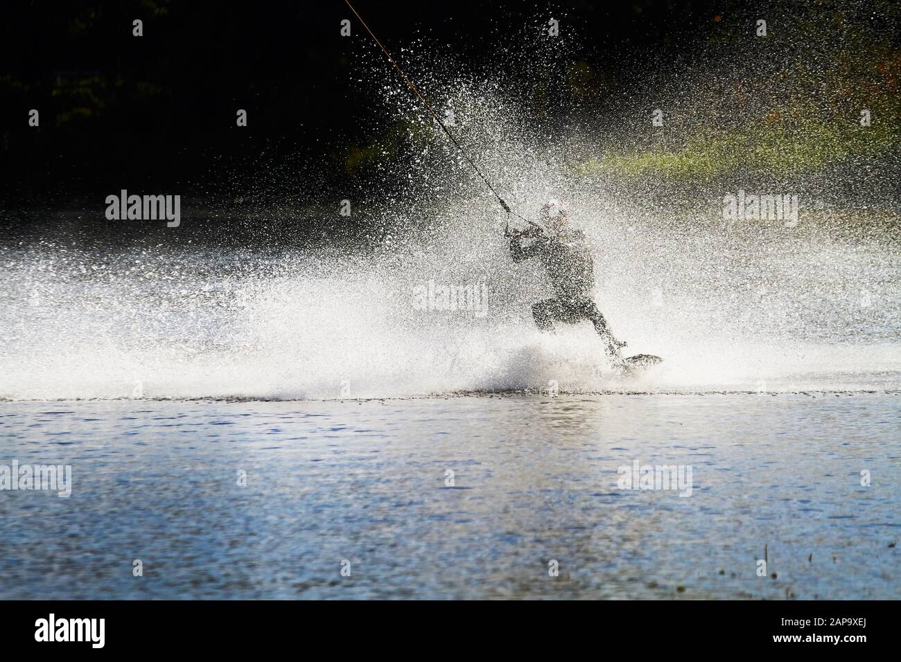 Wakeboarder surfing across a lake with water splashing. This is an extreme sport. Stock Photo