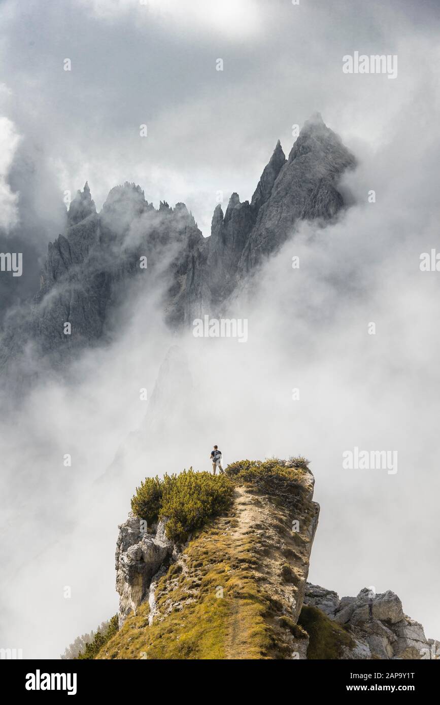 Mountaineer stands on a ridge, behind mountain peaks and pointed rocks, dramatic clouds, Cimon di Croda Liscia and Cadini Group, Auronzo di Cadore Stock Photo