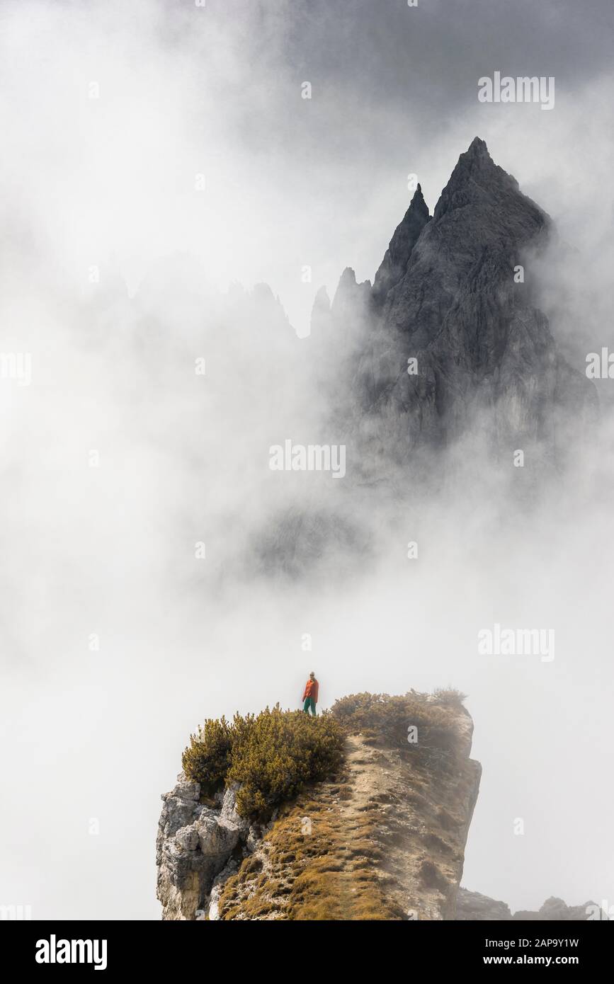 Mountaineer stands on a ridge, behind mountain peaks and pointed rocks, dramatic clouds, Cimon di Croda Liscia and Cadini Group, Auronzo di Cadore Stock Photo