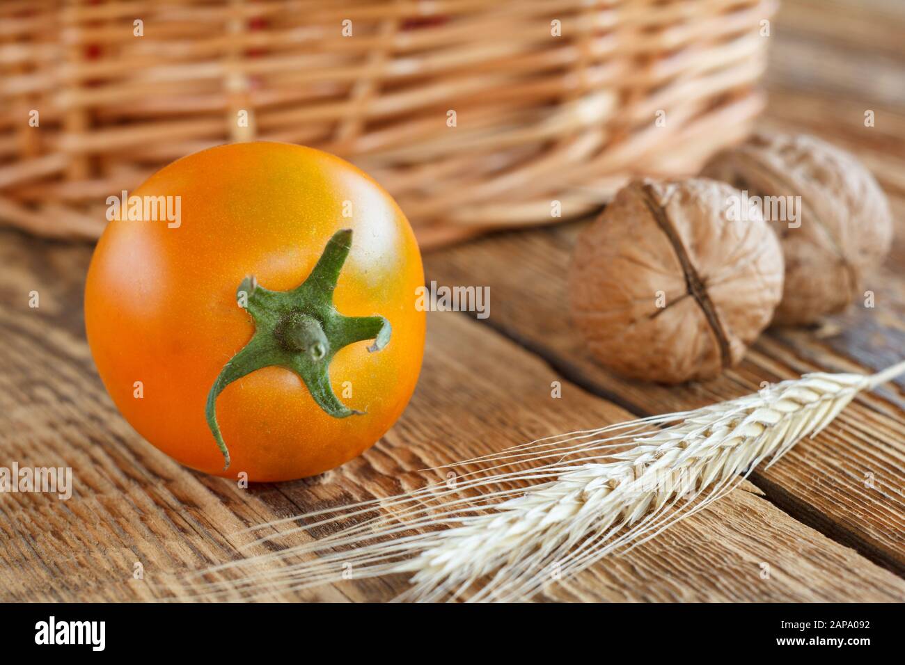 Close-up yellow tomato, walnuts, wheat ears and wicker basket on wooden background. Shallow depth of field. Stock Photo