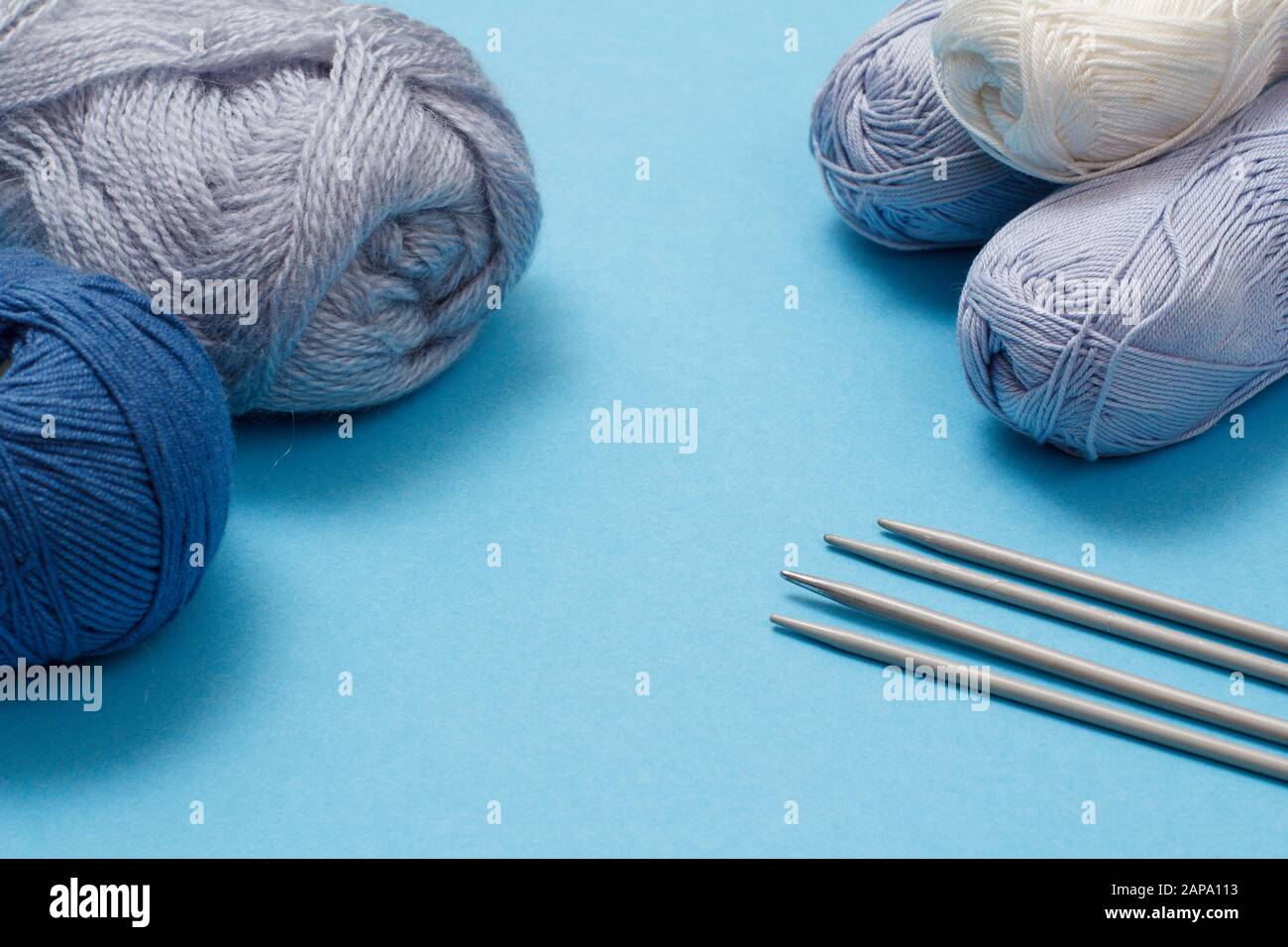 Knitting yarn balls and metal knitting needles on a blue background. Knitting concept. Top view. Stock Photo
