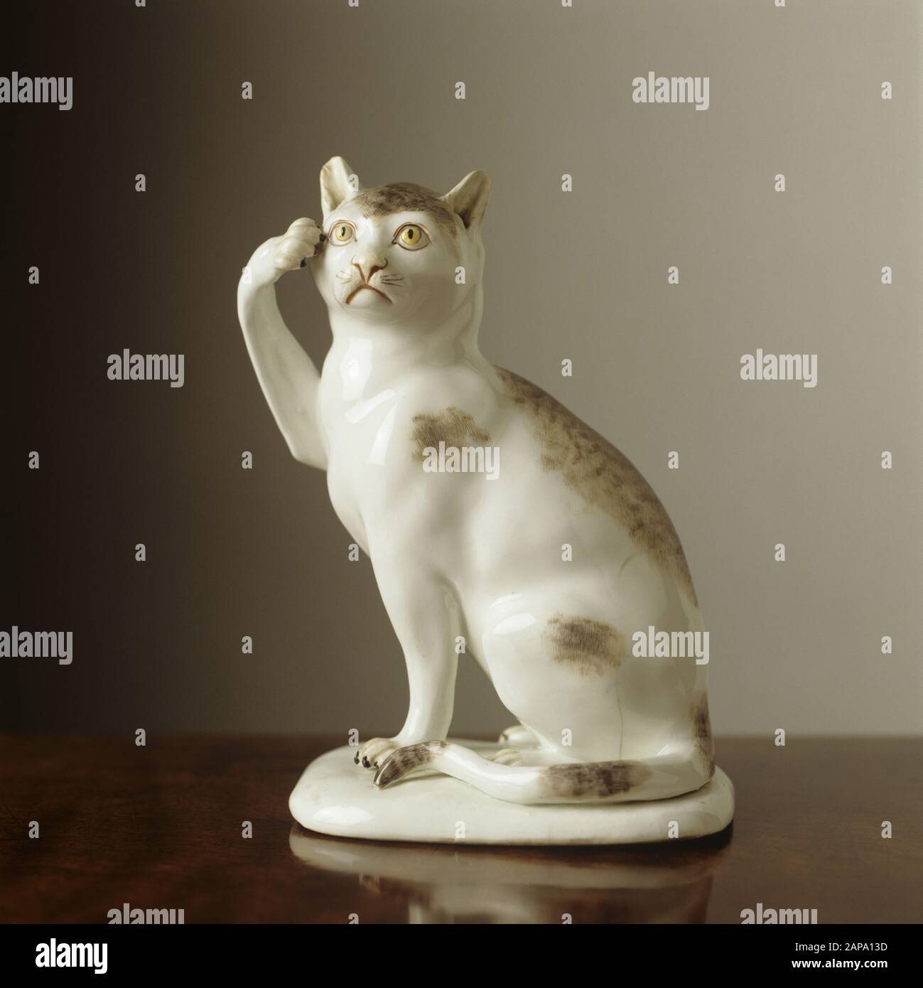 A figure of a seated white porcelain cat with one paw raised to its head. It was made by Meissen c1741-1745 and is found in the Mirror Room. Stock Photo