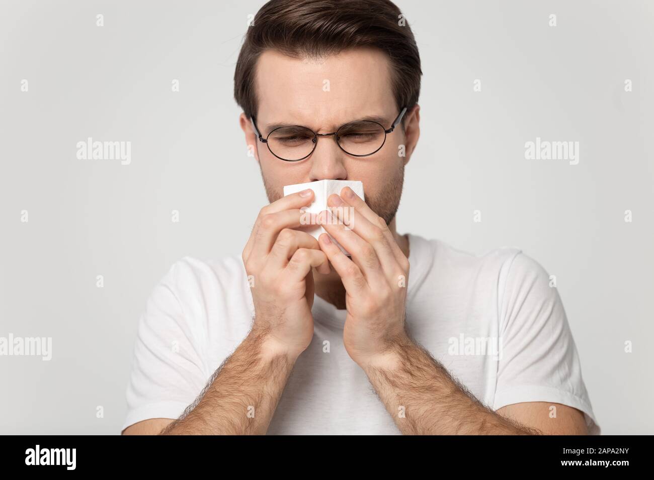 Sick millennial guy caught cold, sneezing, feeling unwell. Stock Photo