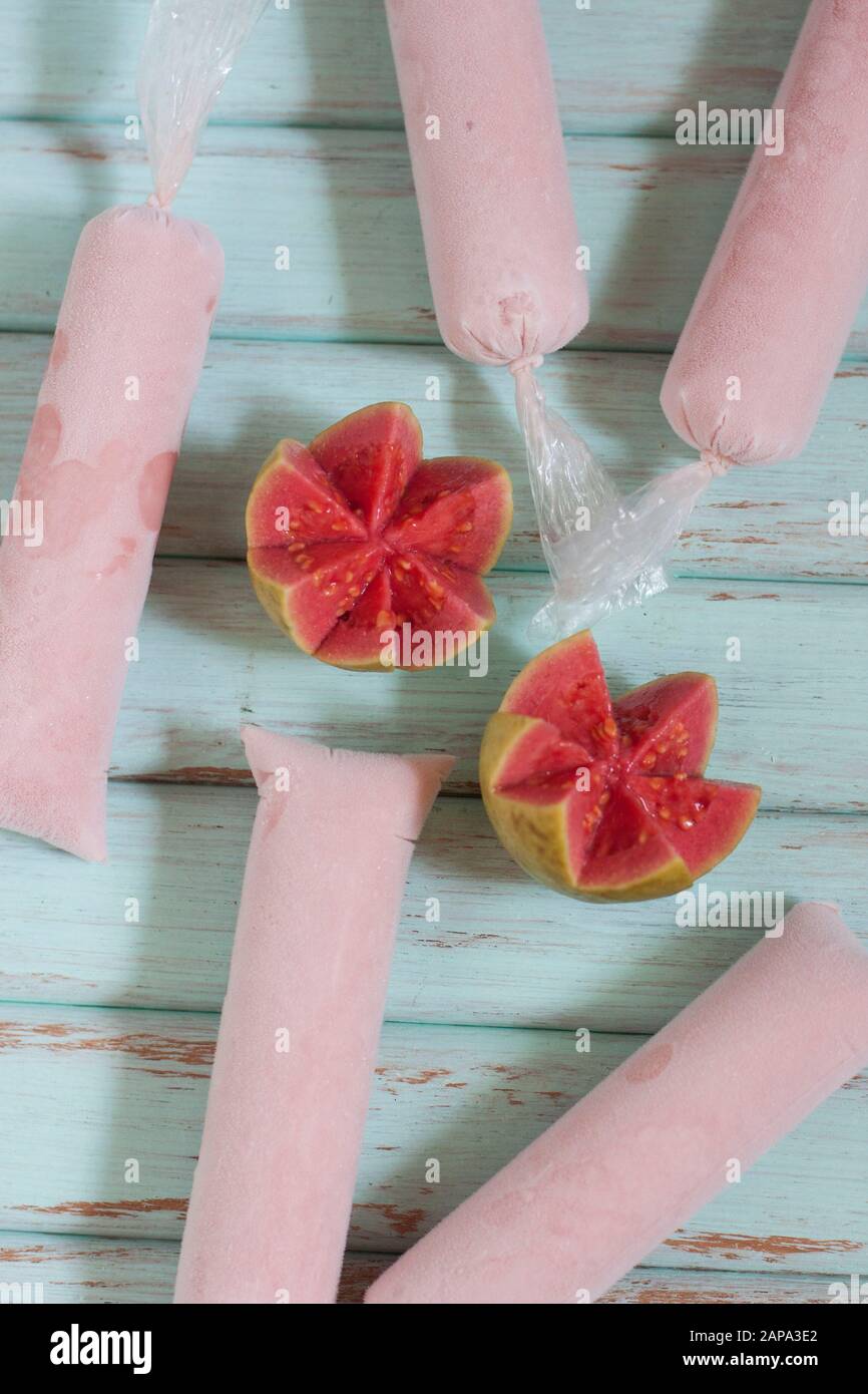 Five pink creamy guava ice lollies on blue backgound with guava fruit cut in half Stock Photo