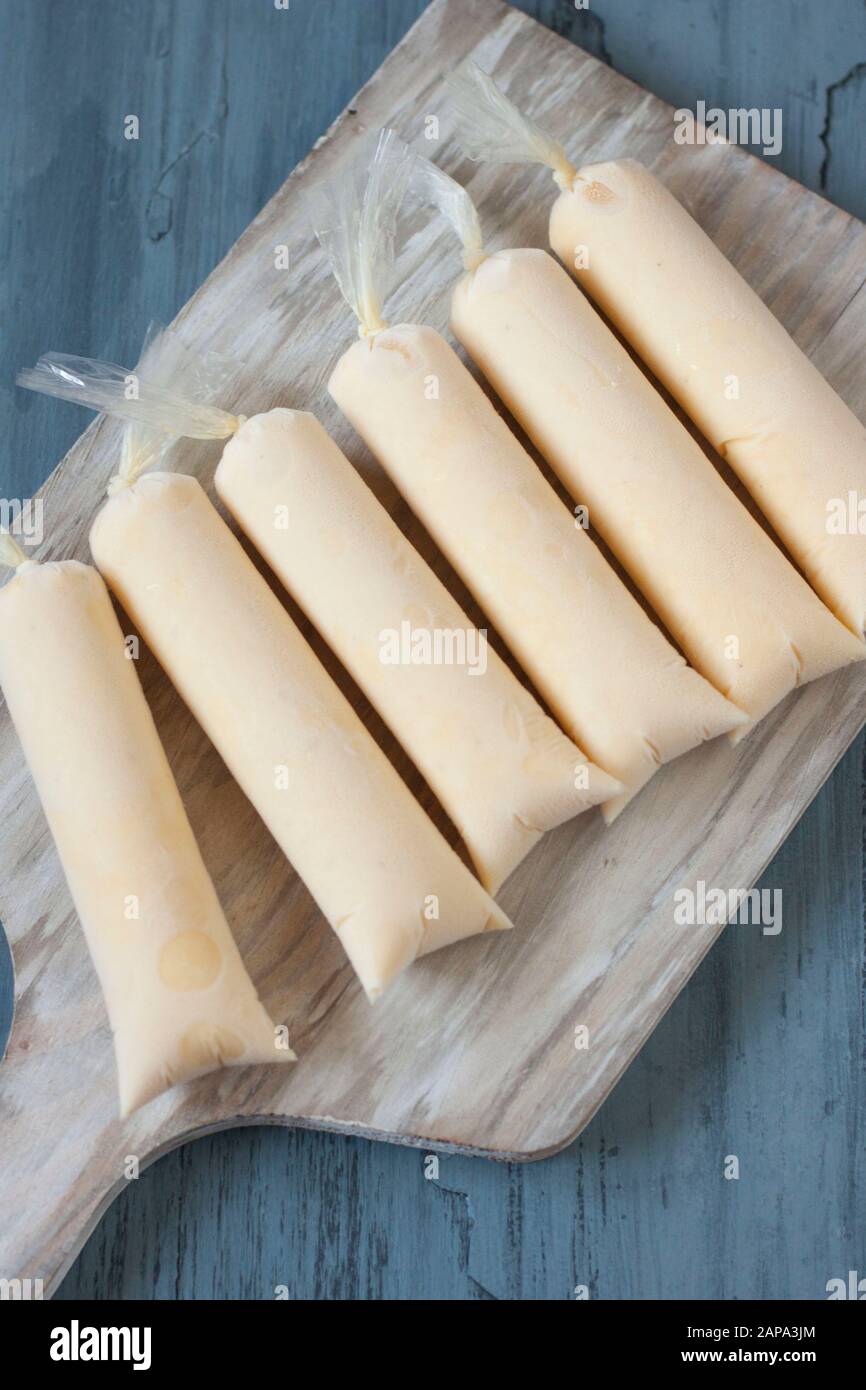 Six light yellow passion fruit ice lollies over whitish board with blue background Stock Photo