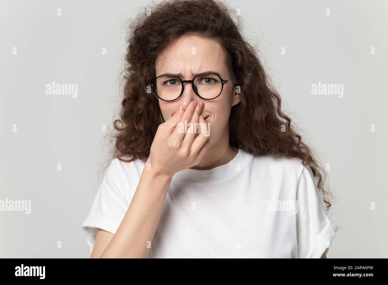 Young curly girl clenching nose, feeling unpleasant smell. Stock Photo