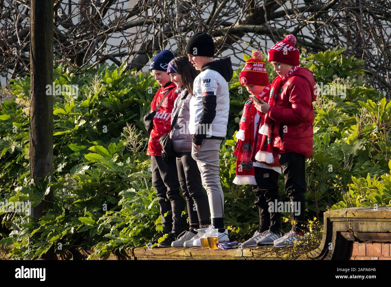Small children wearing LFC colours standing on a wall waiting to greet the arrival Liverpool FC  team coach at Anfield Liverpool. Stock Photo