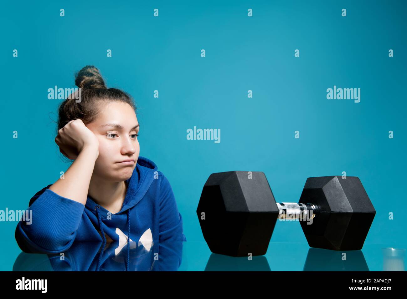 the girl looks in frustration and longing at the big dumbbell lying in front of her, close up Stock Photo