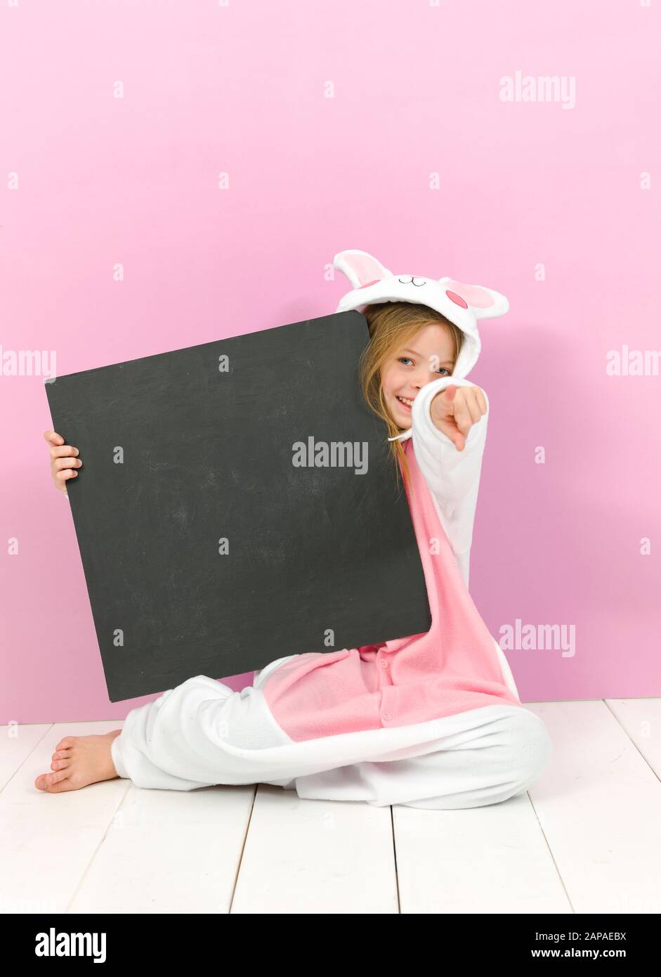 pretty blonde girl with cozy rabbit costume and blackboard is posing in the studio and is happy Stock Photo