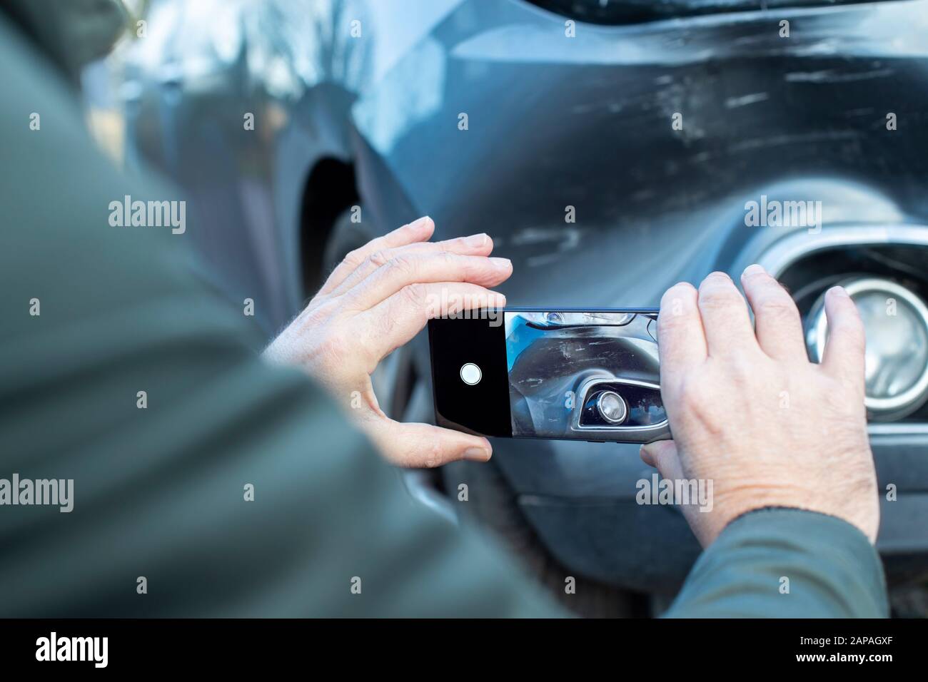 Male Driver Taking Photo Of Damaged Car After Accident For Insurance Claim On Mobile Phone Stock Photo