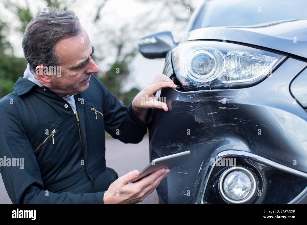 Auto Workshop Mechanic Inspecting Damage To Car And Filling In Repair Using Digital Tablet Stock Photo