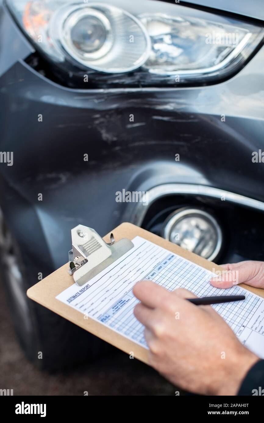 Close Up Of Auto Workshop Mechanic Inspecting Damage To Car And Filling In Repair Estimate Stock Photo