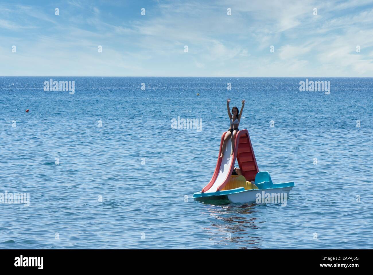 Teen in bathing suit sitting with hands up in the air on paddleboat