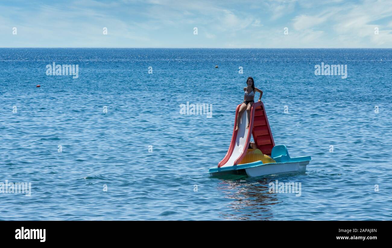 Teen in bathing suit sitting on paddleboat with slide at beach in