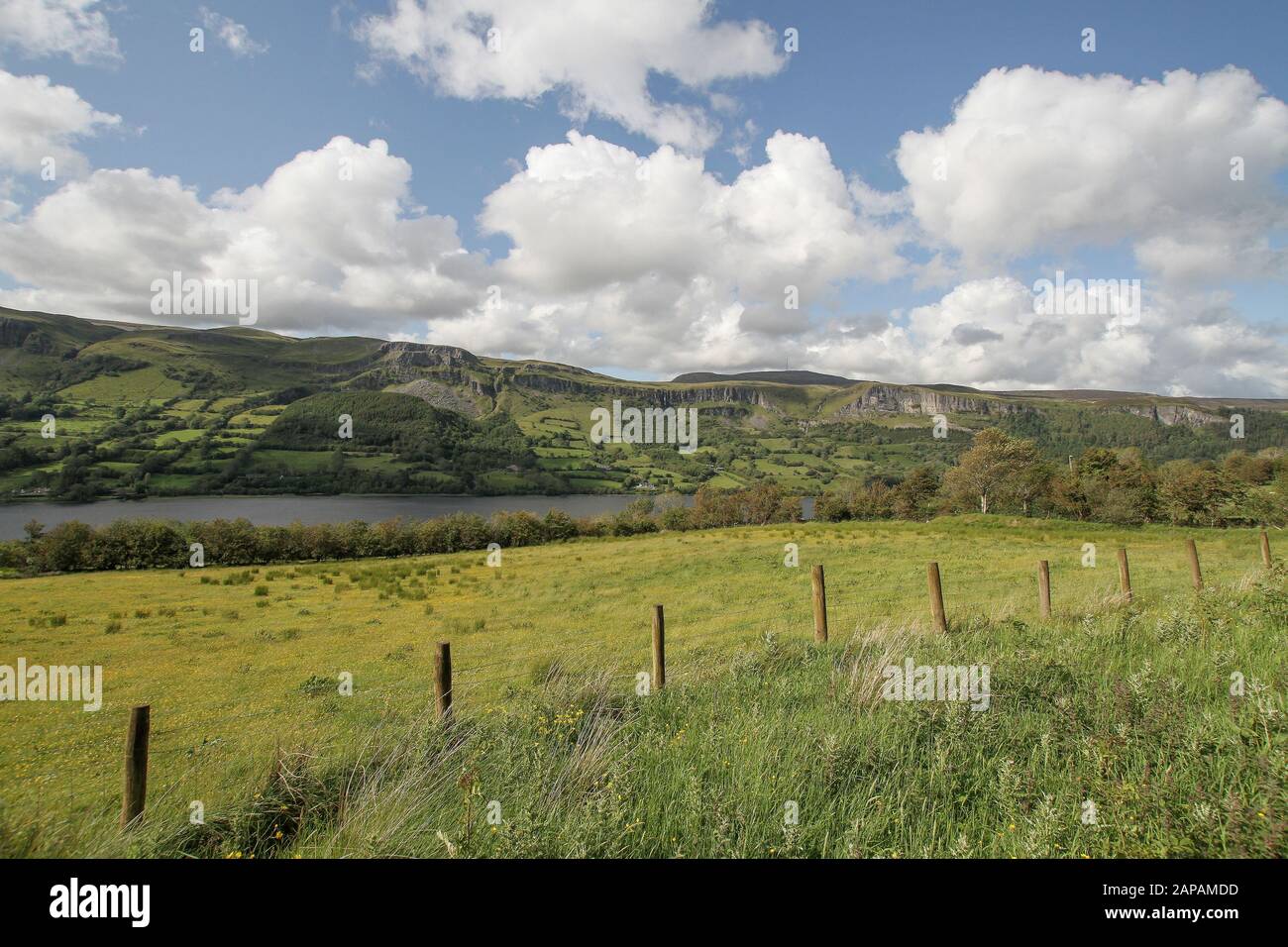 Summer with white clouds and blue sky in rural Ireland with a view beyond the wire fence and green fields across Glencar Lake to the Dartry Mountains. Stock Photo