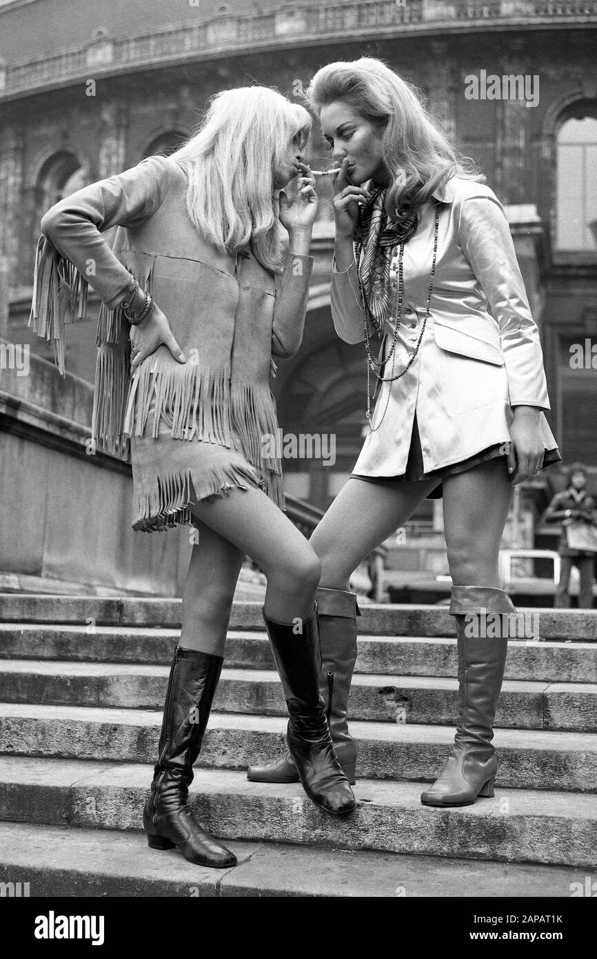 In fringed outfit reminiscent of the old Wild West, Amanda Leah (left), 25, gets a light from Jayne Harries, 17, at the Royal Albert Hall, London, where they attended the Ossie Clark and Alice Pollock's preview of the Christmas Party to be held at the Royal Albert Hall. Stock Photo