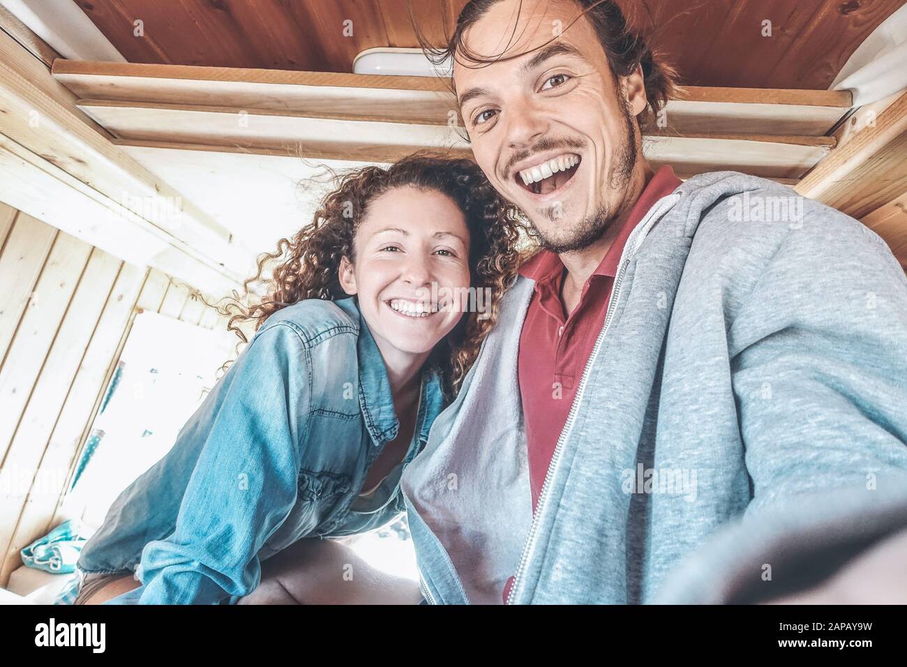 Happy couple taking a selfie in mini van camper during a roadtrip - Travel people having fun making pictures with mobile phone in vintage minivan Stock Photo