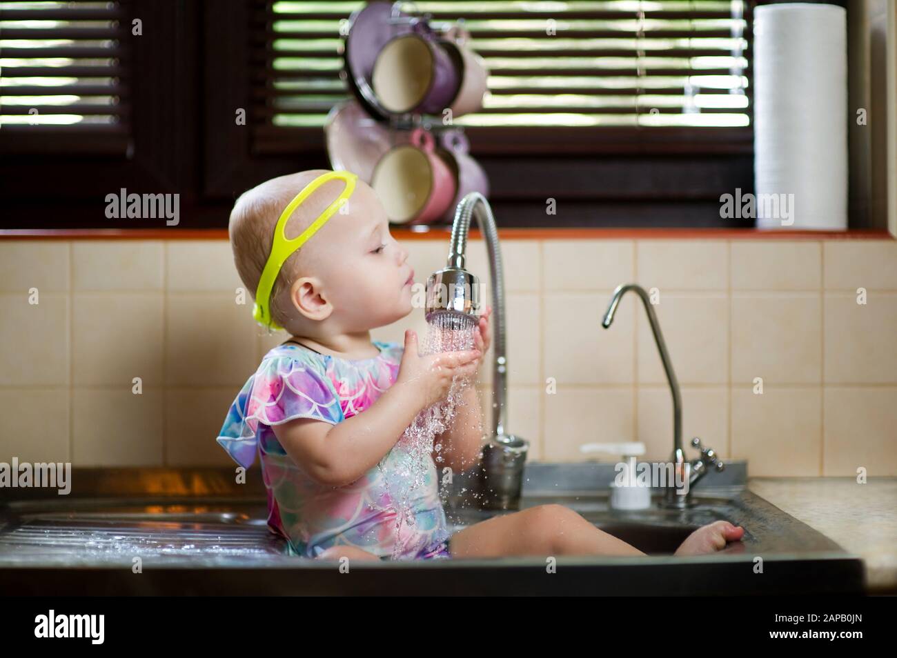 baby splashing in the kitchen sink, having fun with water Stock Photo