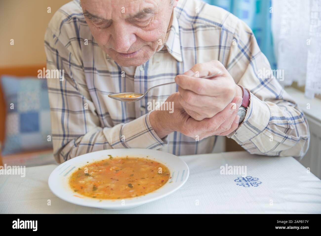 Elderly man with Parkinsons disease holds spoon in both hands Stock