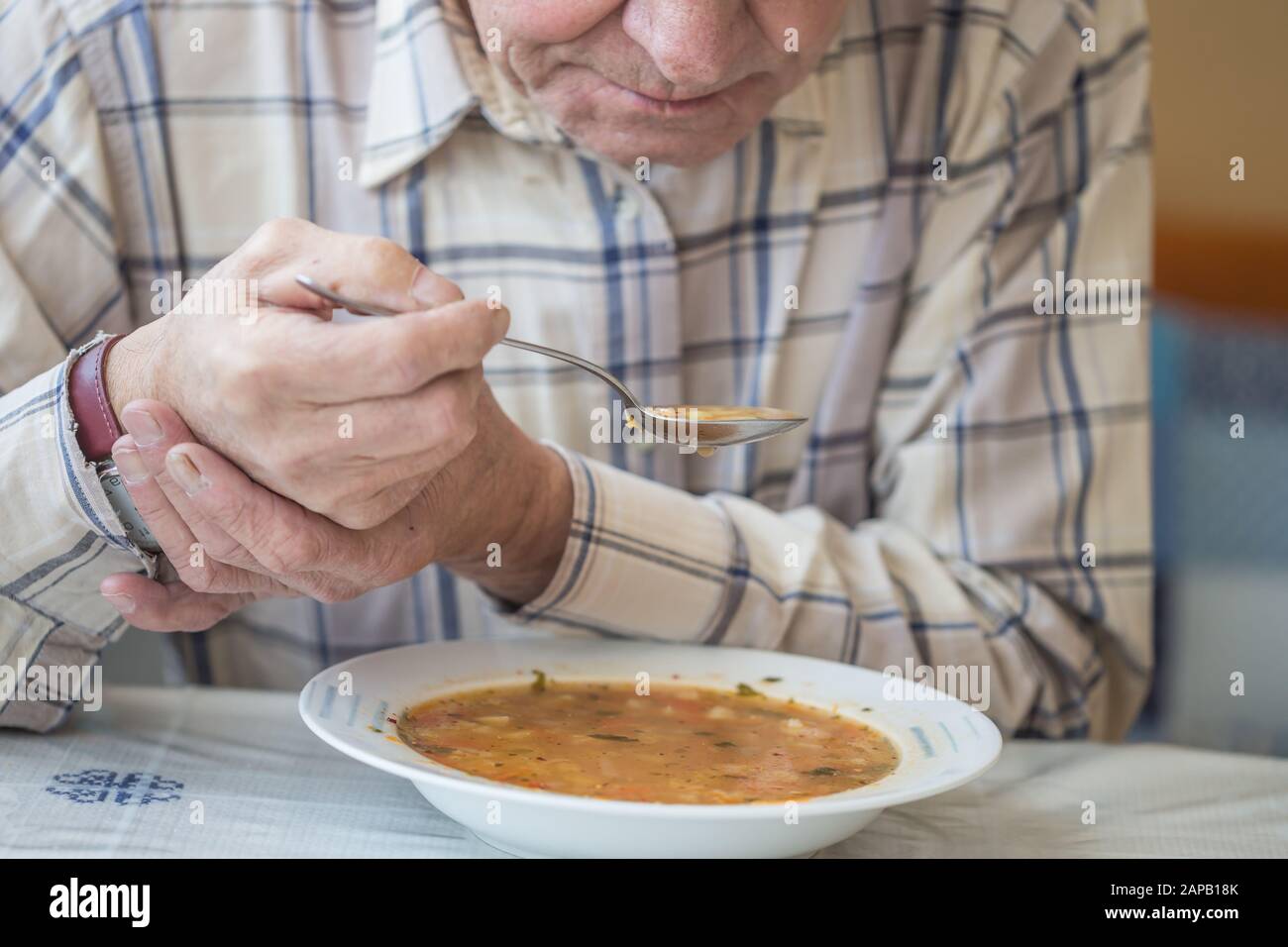 Elderly man with Parkinsons disease holds spoon in both hands Stock