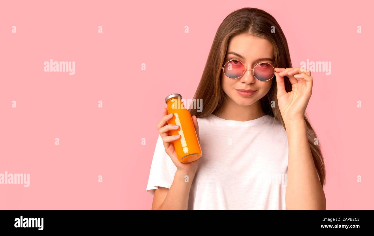 Cheerful and cool woman holding orange detox juice on pink Stock Photo