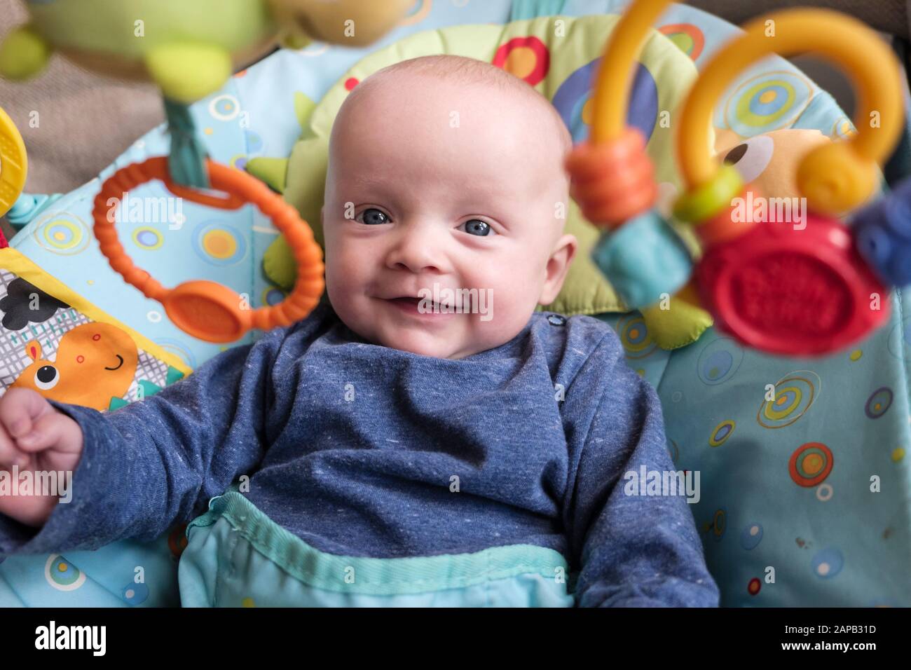 Authentic image of a happy baby boy age five months in an activity chair smiling and looking at