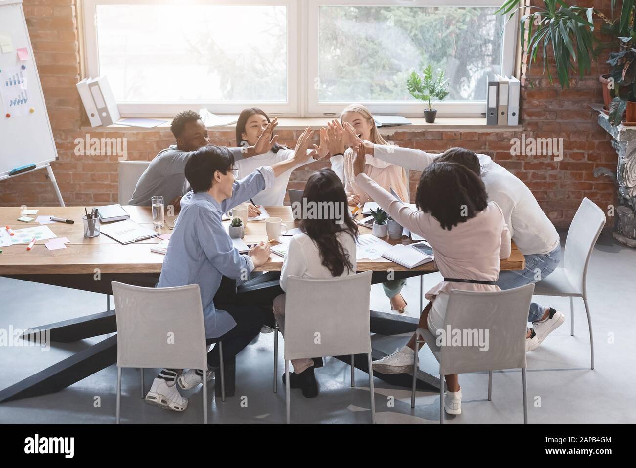 Multiracial business team giving high five in office during meeting ...