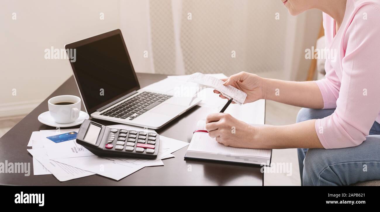 Senior lady writing calculation in notebook with bills Stock Photo