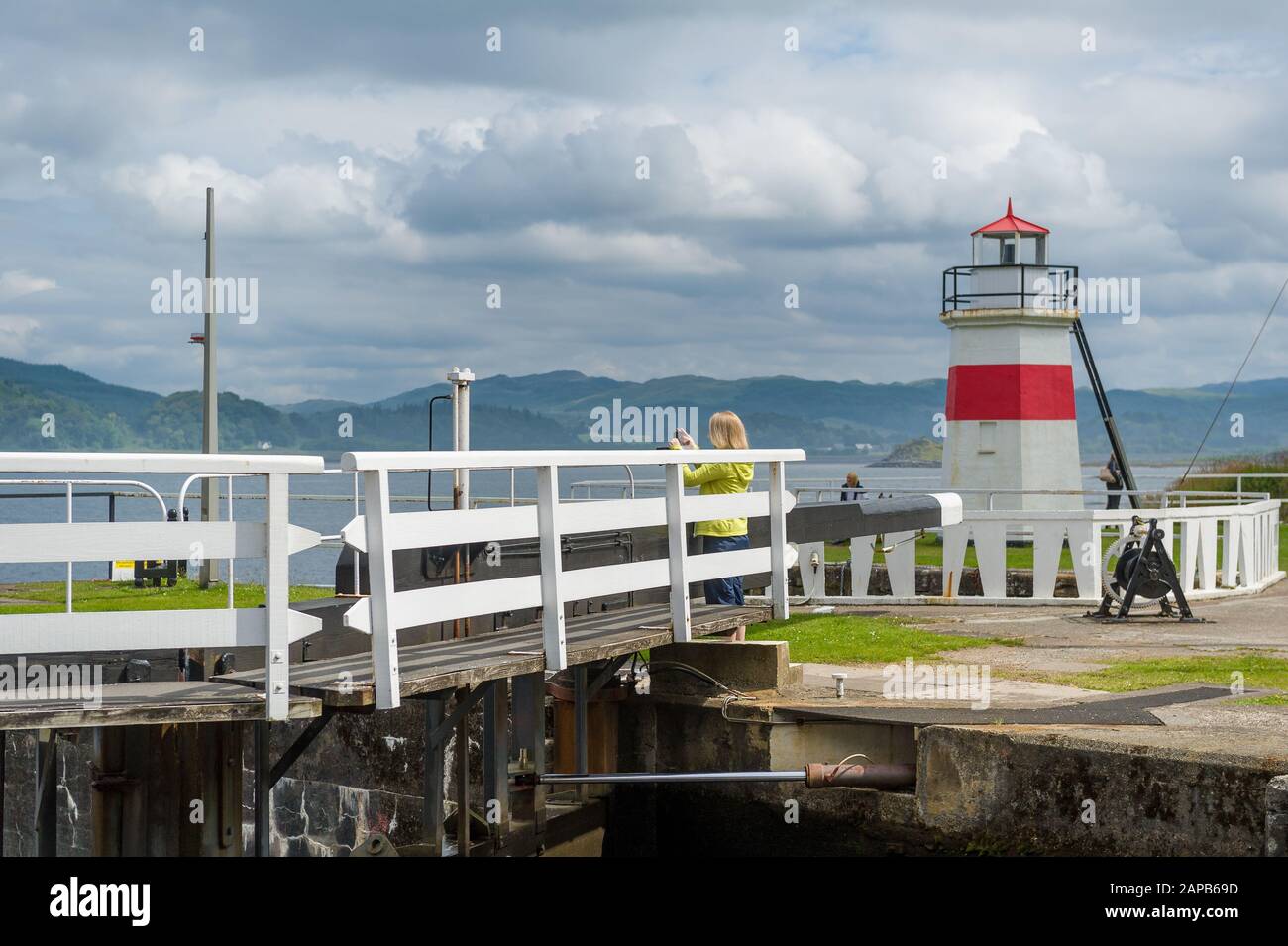 Woman taking pictures at the first bridge of Crinan canal. Sea lighhouse of Crinan. Scotland. Stock Photo