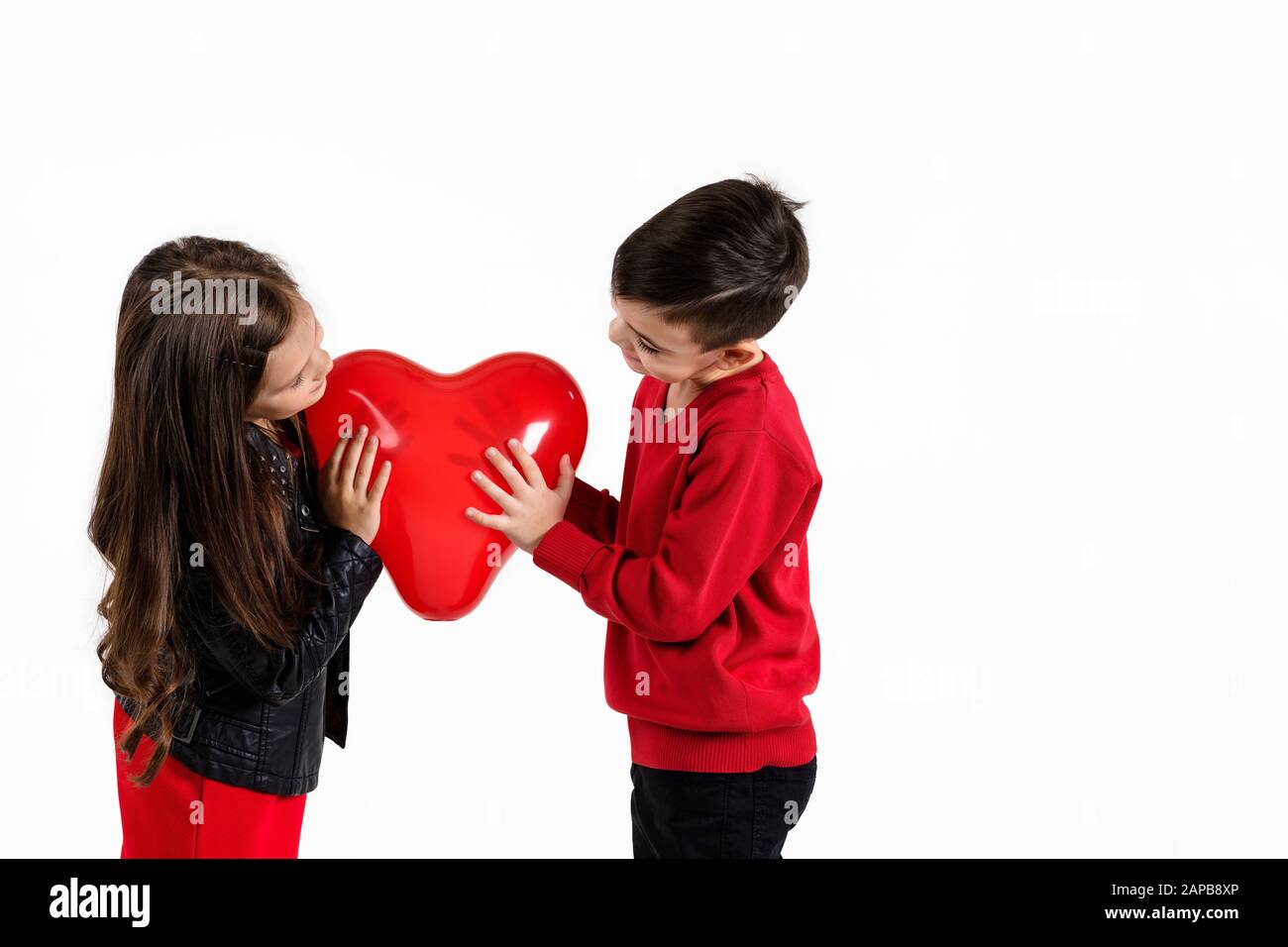 Happy little couple girl and boy holding red heart balloon together