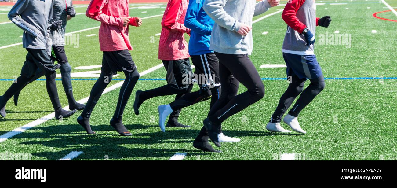 High school boys take their shoes off and jog on the turf in their socks on a sunny, but cold winter afternoon. Stock Photo