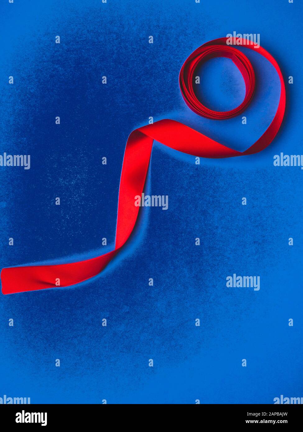 red silk ribbon twisted on a trendy classic blue background, festive postcard, copy space Stock Photo