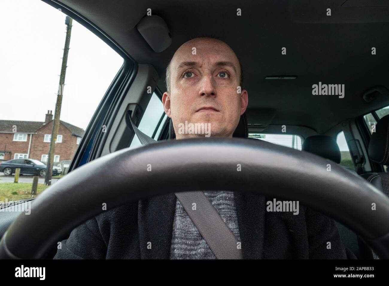 A middle aged man sat behind a steering wheel in the driver's seat of a