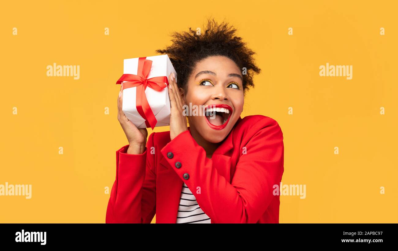 Happy black girl shaking gift box near ear Stock Photo - Alamy