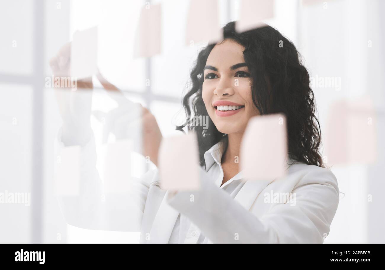 Smiling brazilian manager writing on sticky notes on window Stock Photo ...