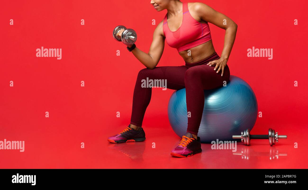 Sporty girl exercising with barbells, sitting on fitness ball Stock Photo