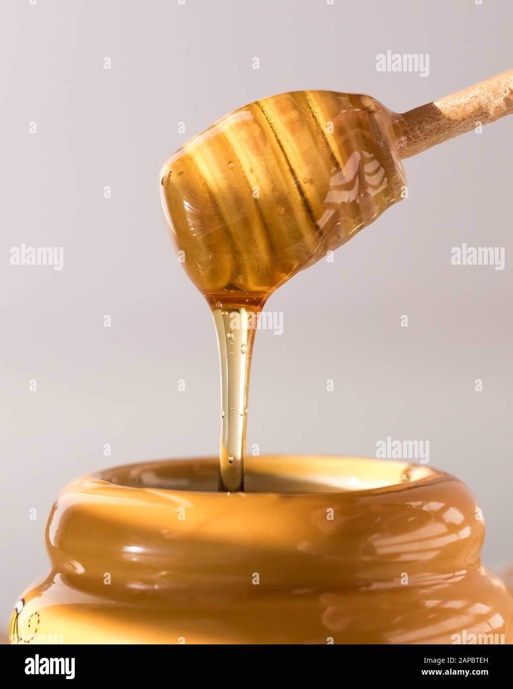 A close up view of a honey dipper dripping with honey into a honey pot