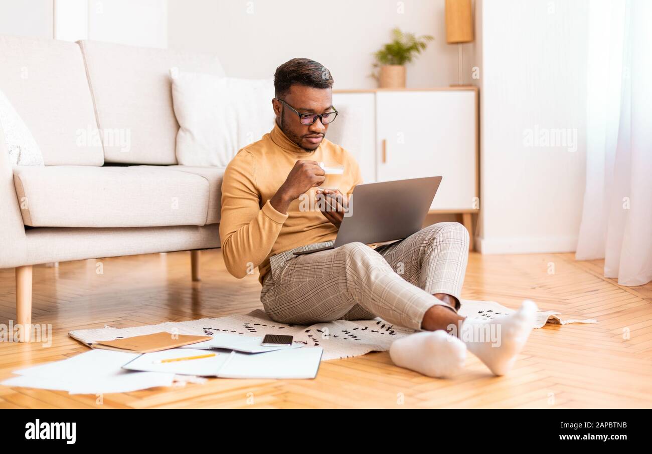 Afro Man Working On Laptop Having Coffee Sitting On Floor Stock Photo