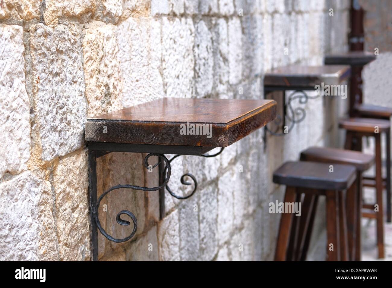 Bar wooden table with iron mount in outdoor summer veranda of coffee house. Wall of old bright textured stone in background. Stock Photo