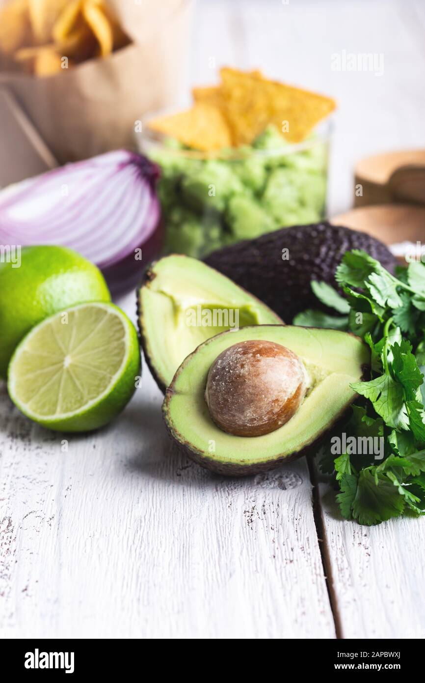 Mexican traditional food, guacamole sauce ingredients  avocado, red onion, cilantro, lime and tortilla corn chips on white rural table. Preparing loca Stock Photo